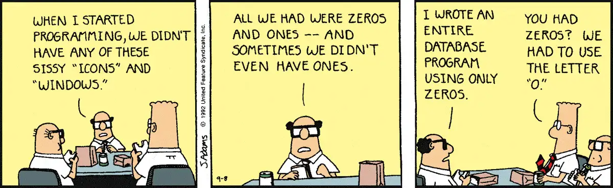 A three-panel Dilbert comic strip. In the first panel, a bald coworker with glasses tells Dilbert and another coworker at a lunch table that when he started programming, they didn't have any "sissy 'icons' and 'windows'." In the second panel, he continues with a serious expression, stating that all they had were zeros and ones, and sometimes they didn't even have ones. In the third panel, Dilbert sarcastically replies, "You had zeros? We had to use the letter 'O'."